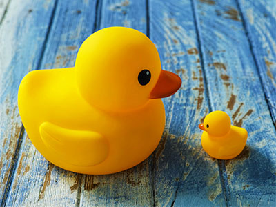 Two rubber ducks, one big and one small face each other as if talking together. Conceptual image realting to different points of view, intimidation, underdog, parent with child, advice. The ducks are sitting on an old weathered wooden background representing conceptual water.