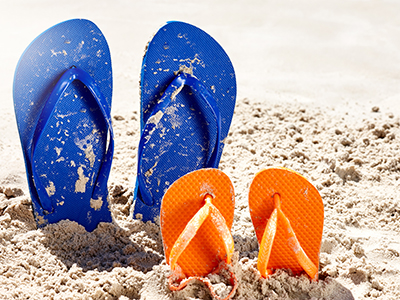 Two pairs of flip flops - one adult, one for a child, are stuck in the sand on a beach. Vacation time.