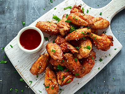 Baked chicken wings with sesame seeds and sweet chili sauce on white wooden board