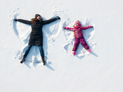 Child girl and mother playing and making a snow angel in the snow. Top flat overhead view