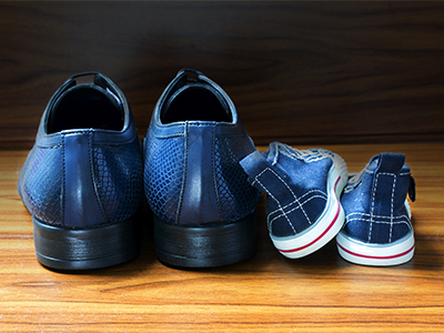 Men shoes and children sneakers from behind side by side on the wooden floor, concept of family, at home and father's day